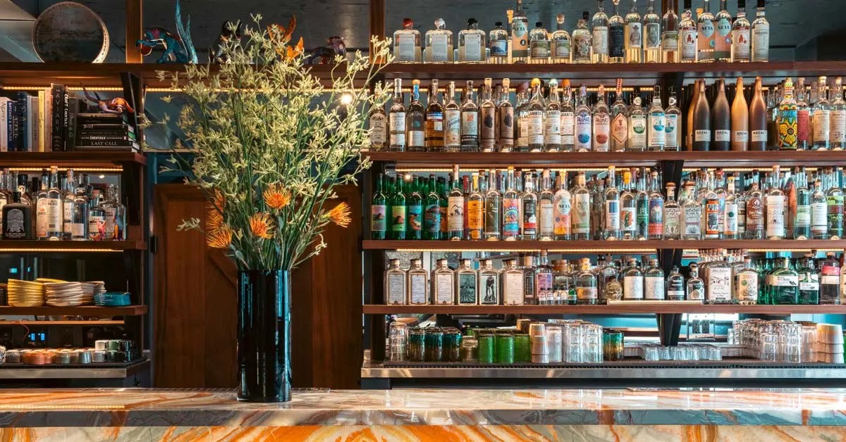 A marble bar. Behind it there’s a shelf full of liquor bottles.