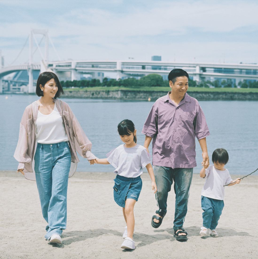 家族4人が手を繋いで砂浜を歩いている。