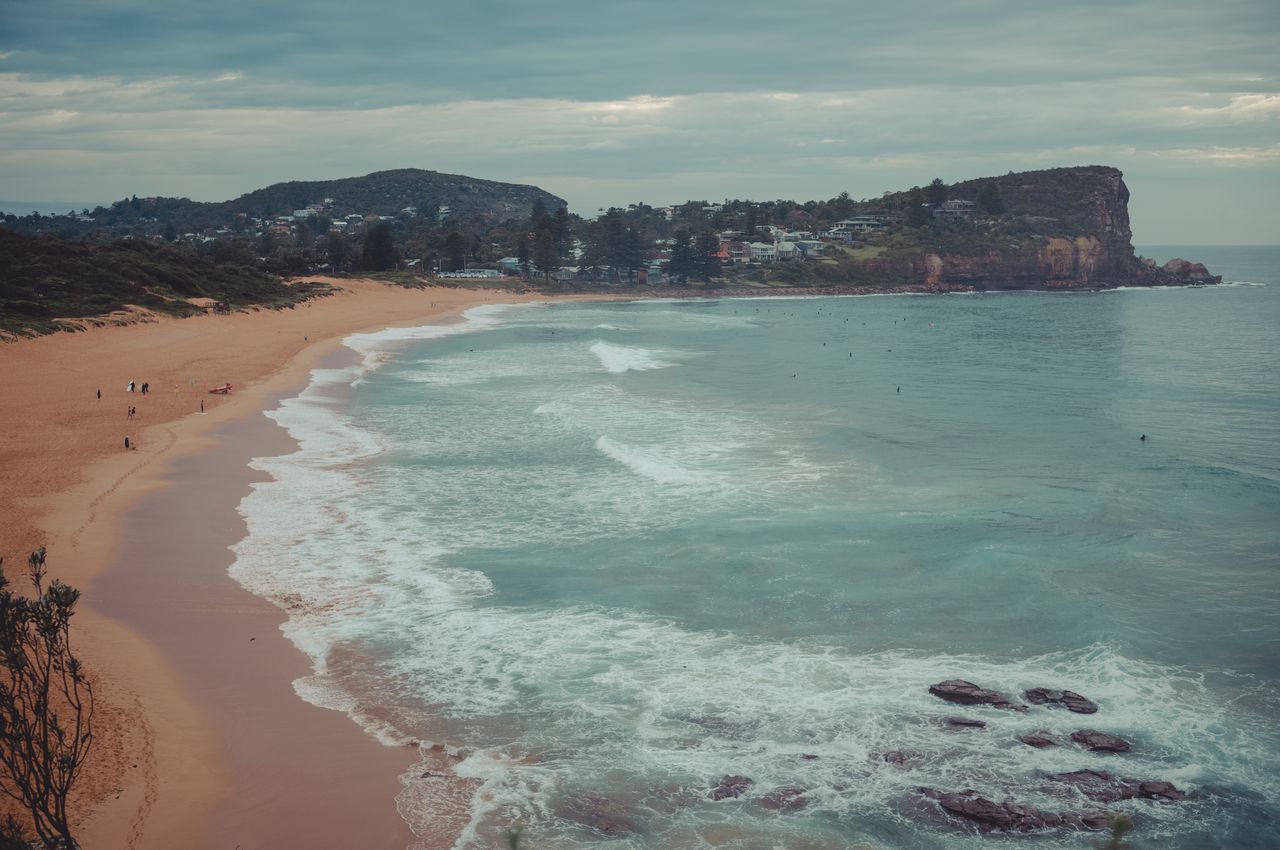 Aerial view of a beach with a sandy shoreline, rolling waves, and  prominent cliffs in the distance.