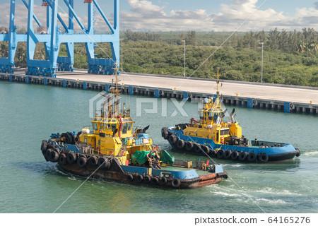 Tug boats awaiting big cargo ship in harbour for 64165276