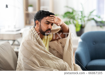 sick young man in blanket having headache or fever 66867105