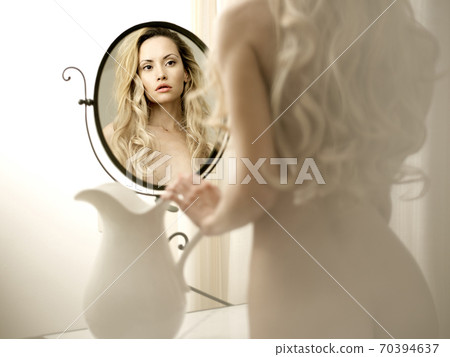 Nude elegant blonde woman pose in front of the mirror. 70394637