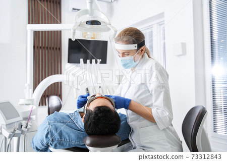 Friendly dentist adjusting something while working in dental clinic 73312843