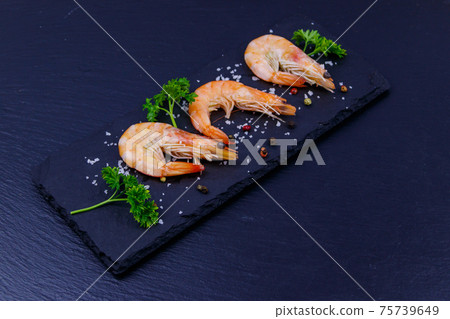 Big raw red prawns with parsley, salt and pepper on a slate board on black background 75739649