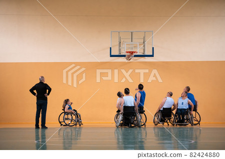 Disabled War veterans mixed race opposing basketball teams in wheelchairs photographed in action while playing an important match in a modern hall.  82424880