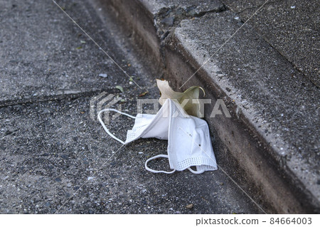 Non-woven white mask abandoned on asphalt road 84664003