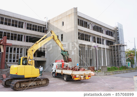 Heavy equipment for loading rubble from a demolition dilapidated public building onto a truck with a crane 85708899