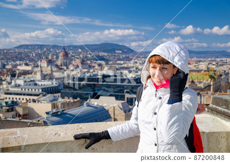 Young woman traveler with white jacket, red scarf and backpack looking away at distance 87200848