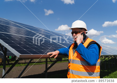 Male engineer in hardhat standing near solar panels and talking on the phone 89571638