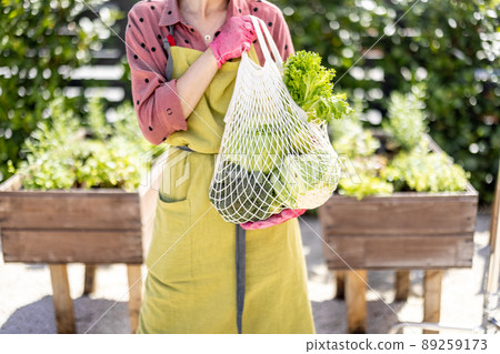 Holding mesh bag full of fresh vegetables and greens at home garden 89259173