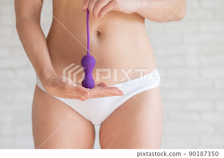 Faceless woman in white panties and with a bare tummy holds a kegel trainer. Latex vaginal vibrator for training the pelvic floor muscles with an antenna. The device for imbuilding. Women Health. 90187350