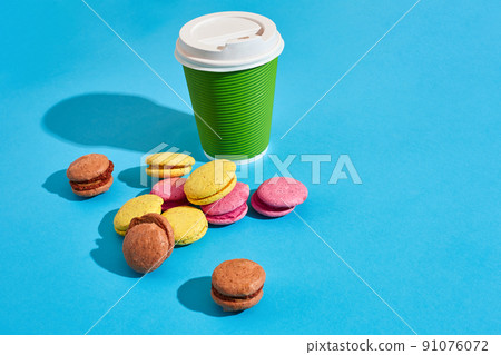 Hot coffee in green paper cup with white lid and macaroons on bl 91076072