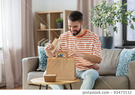 smiling man unpacking takeaway food at home 93473532