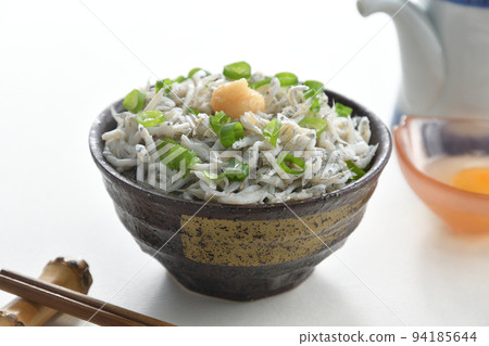 Whitebait rice bowl topped with ginger, chopsticks, soy sauce jug and raw egg (white background) 94185644