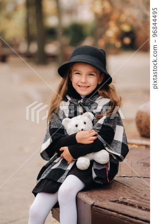 A little stylish girl in autumn clothes is sitting on a bench in the autumn city 96844495