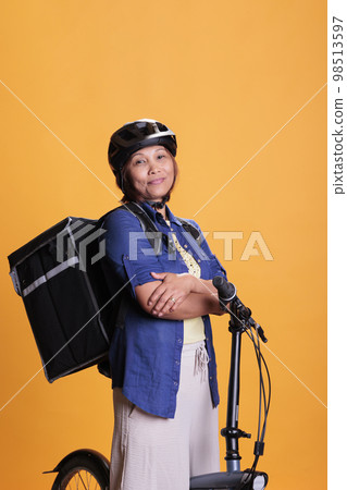 Smiling takeaway delivery person carrying thermal takeout food backpack, delivering pizza meal from restaurant. Asian bicyclist wearing helmet during deliver job, home delivery service 98513597