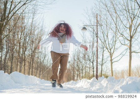 Smiling plump redhead woman jumping in park in winter.  98819924