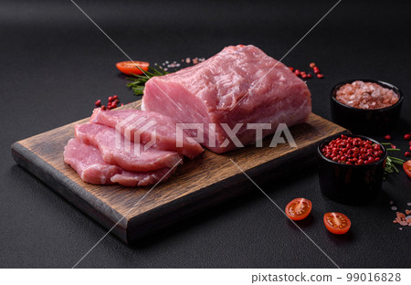 A piece of raw fresh pork on a wooden cutting board with spices and herbs 99016828