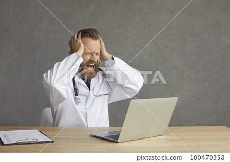 Tired stressed crazy doctor crying sitting at desk with computer in medical office 100470358