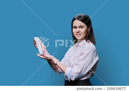 Young woman holding empty tube with cosmetic product on blue background 100656677