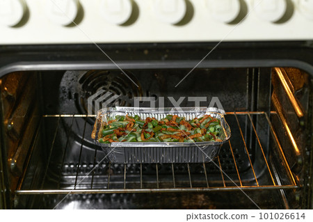 green bean casserole sprinkled with crispy fried onions in a aluminum food box in the oven, selective focus. 101026614