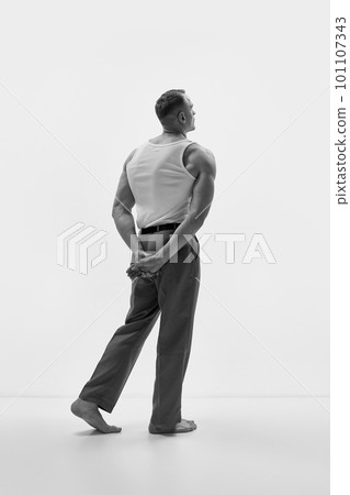 Studio shot of elegant man wearing classic trousers and posing over studio background. Muscular body shape. Black and white 101107343