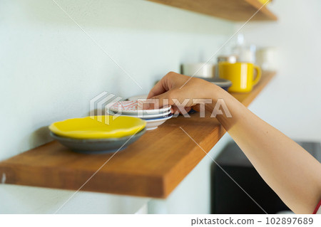 A woman's hand arranging dishes on the shelf 102897689