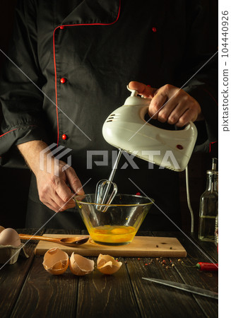 Delicious breakfast by the hands of the chef in the kitchen. Cooking an egg omelette with a hand-held electric mixer 104440926