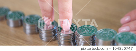 Businesswoman fingers walking on pile of coins at desk. 104830747