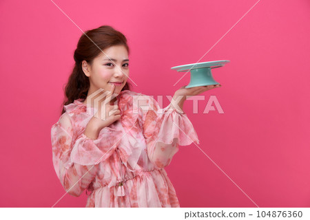 female model wearing a flower-patterned dress with a pink background and holding a cake plate 104876360