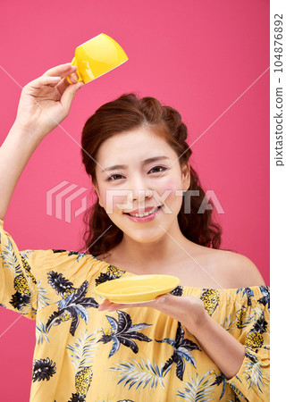 female model wearing a flower-patterned dress with a pink background and posing with a yellow coffee cup 104876892