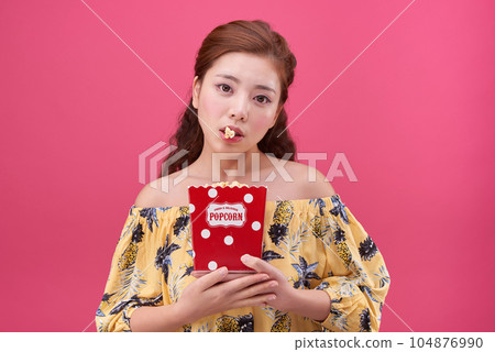 female model wearing a flower-patterned dress with a pink background and eating popcorn deliciously 104876990