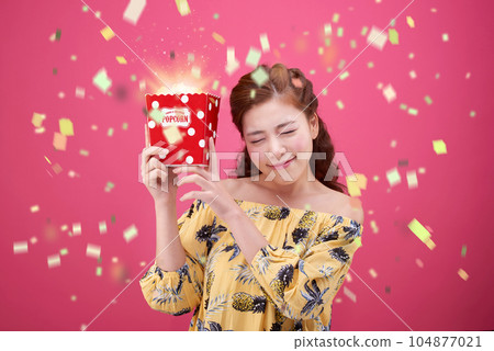 female model wearing a flower-patterned dress with a pink background and eating popcorn deliciously 104877021