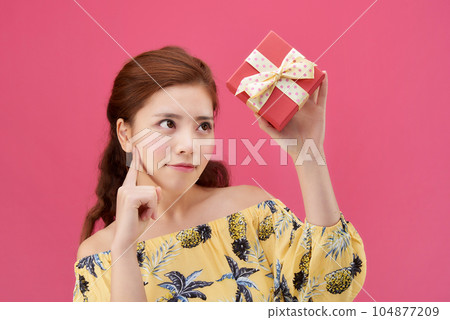 female model wearing a flower-patterned dress with a pink background and posing with a red gift box 104877209