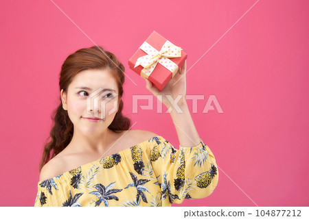 female model wearing a flower-patterned dress with a pink background and posing with a red gift box 104877212