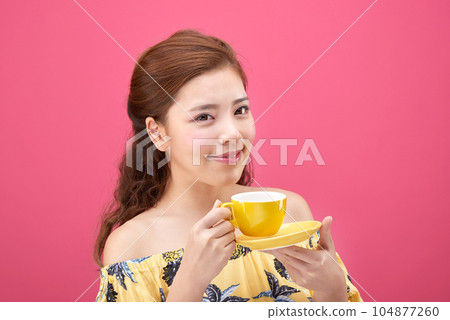 female model wearing a flower-patterned dress with a pink background and posing with a yellow coffee cup 104877260