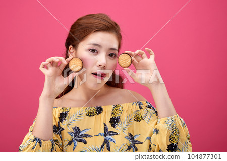 female model wearing a flower-patterned dress with a pink background and enjoying snacks 104877301