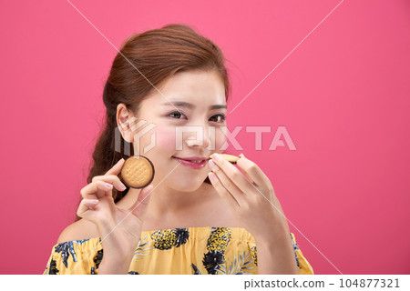 female model wearing a flower-patterned dress with a pink background and enjoying snacks 104877321