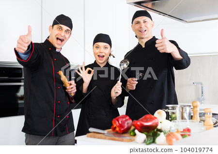 Two men and woman kitcheners in uniform are standing with devices in the kitchen 104019774