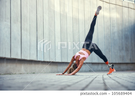 Balance and flexibility. Full-length of young disabled woman with leg prosthesis in sportswear doing yoga asana outdoors. Disabled sport concept 105689404