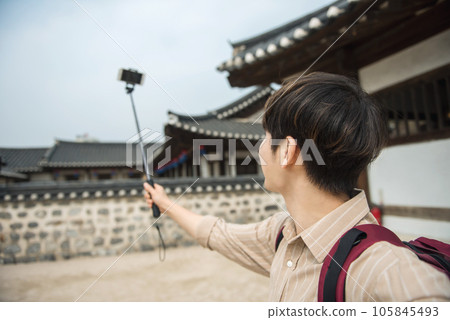 A young man traveling around a traditional village and taking pictures with a smartphone camera 105845493