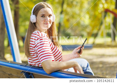 A woman wearing headphones listening to music while sitting on a bench 105142611