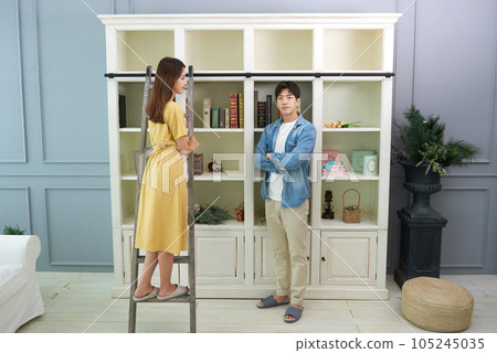 a young couple arranging books on the bookshelf in the living room 105245035