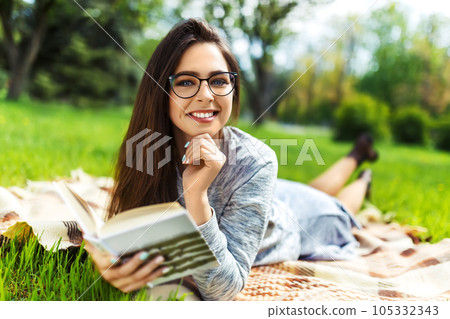 Beautiful relaxed woman readingbook at lawn with sun shining. Girl gets pleasure from reading book. 105332343