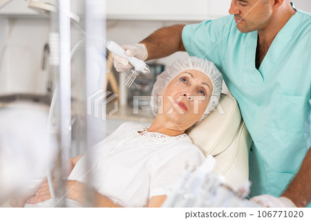 Male dermatologist performing cosmetology procedure for elderly woman, RF lifting and deep hydration for facial skin therapy 106771020