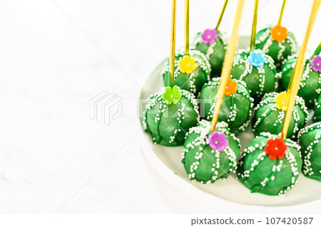 Cactus-shaped cake pops, beautifully decorated with luster dust, sugar flowers, and white sprinkles, arranged in celebration of Cinco de Mayo. 107420587