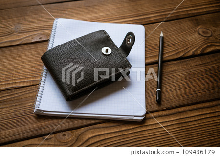 the wallet lies on a notepad with a hand on a wooden table top view 109436179