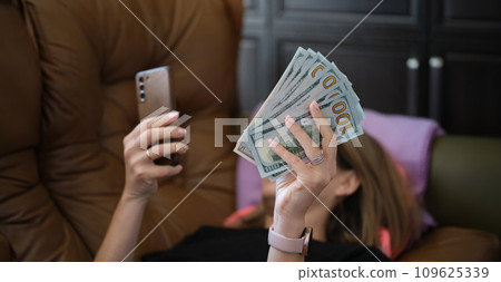 Woman holds smartphone and holds it with dollars 109625339