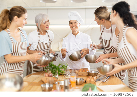 Elderly woman chef with bowl in hands tells women at culinary courses about traditions of cuisine 109872502