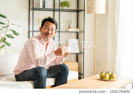 A senior man drinking coffee in the living room. 109276800